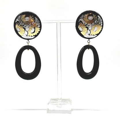 Pair of earrings with floral design and black oval shapes on a clear stand.