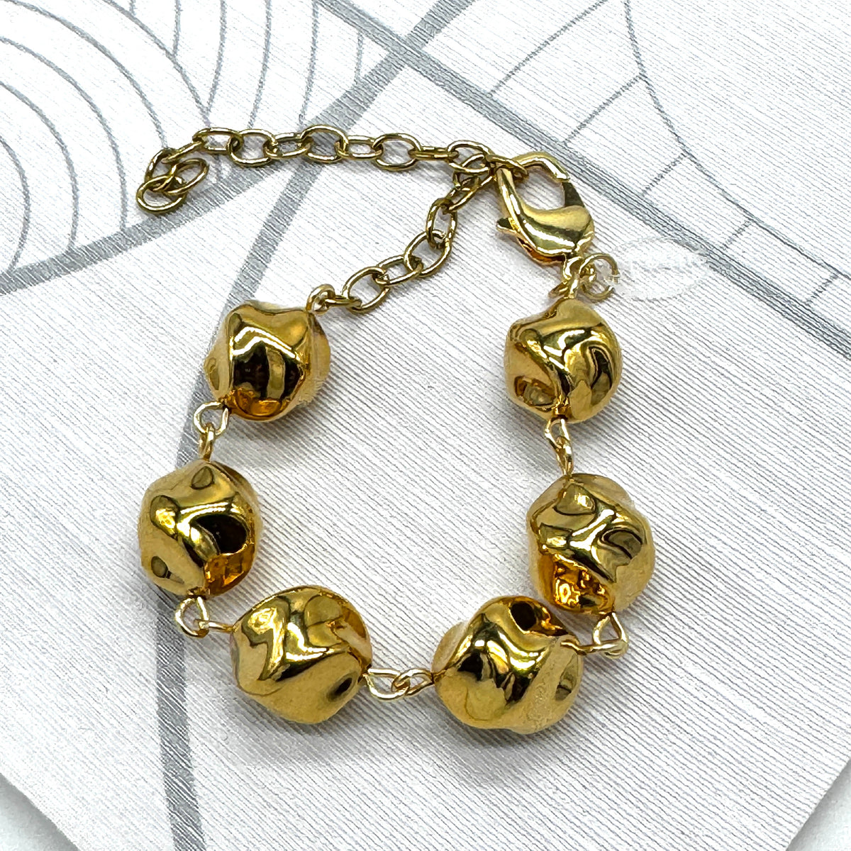 A gold-tone chain bracelet with six irregular, textured bead-like links, displayed on a light gray patterned surface.